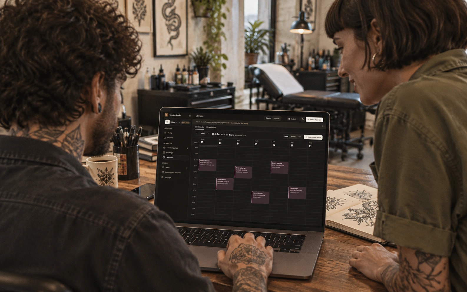 Two tattoo artists planning the week with the English booking calendar on a laptop